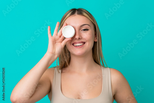 Young caucasian woman isolated on blue background with moisturizer and happiness