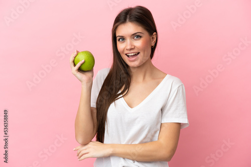 Young caucasian woman isolated on pink background with an apple and happy