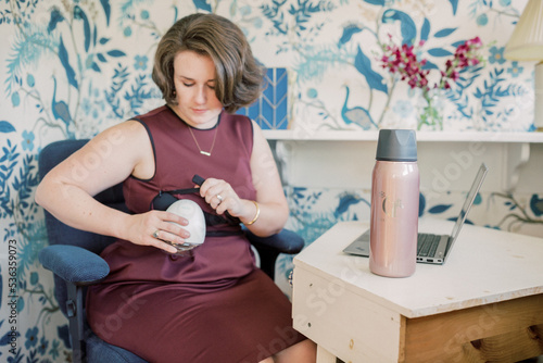 Working at home mother inserts cordless breast pump at desk. photo