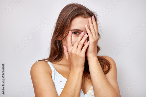 A beautiful girl covers her face with her hands, looking into the slit with one eye.