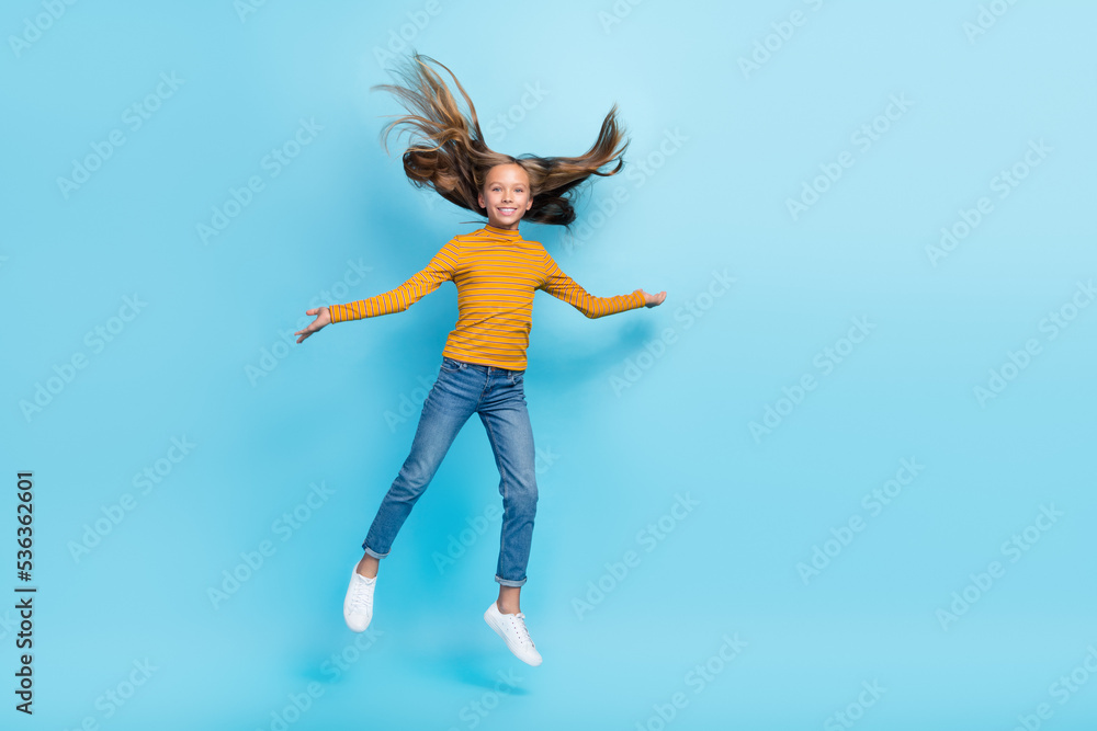 Full body portrait of overjoyed energetic schoolkid jumping flying hair isolated on blue color background Full body portrait of overjoyed energetic schoolkid jumping flying hair isolated on blue color background