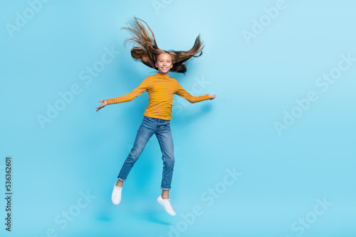 Full body portrait of overjoyed energetic schoolkid jumping flying hair isolated on blue color background