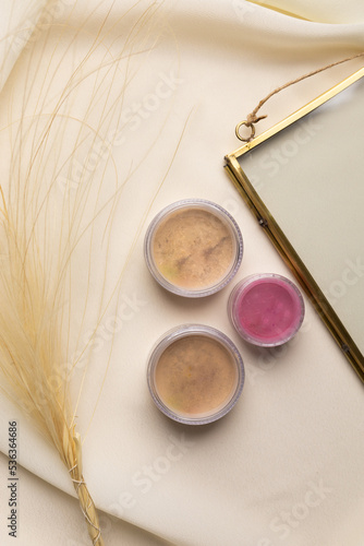 Cosmetics facial powder and blush for cheeks on natural background with dried flowers. Makeup accessories top view