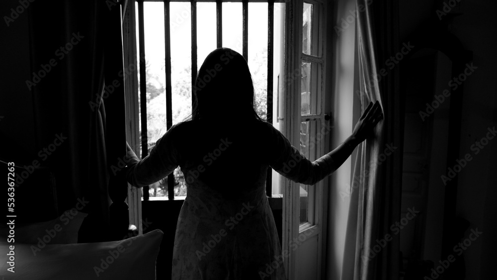 Black and white image of woman holing window curtain and looking outside of window of a rajbari. Black and white image of woman holing window curtain and looking outside of window of a rajbari.