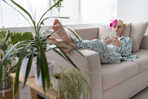 Young pink haired woman relaxing on sofa and reding ebook or social media or serfing internet photo