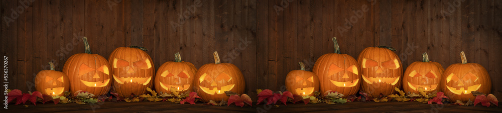 Obraz premium Scary Halloween celebration holiday party card background banner panorama - Many spooky carved glowing pumpkins, jack o lanterns and colorful fallen leaves on wooden table and wall