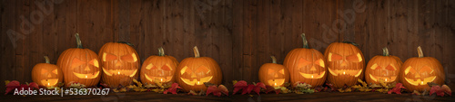 Scary Halloween celebration holiday party card background banner panorama - Many spooky carved glowing pumpkins, jack o lanterns and colorful fallen leaves on wooden table and wall