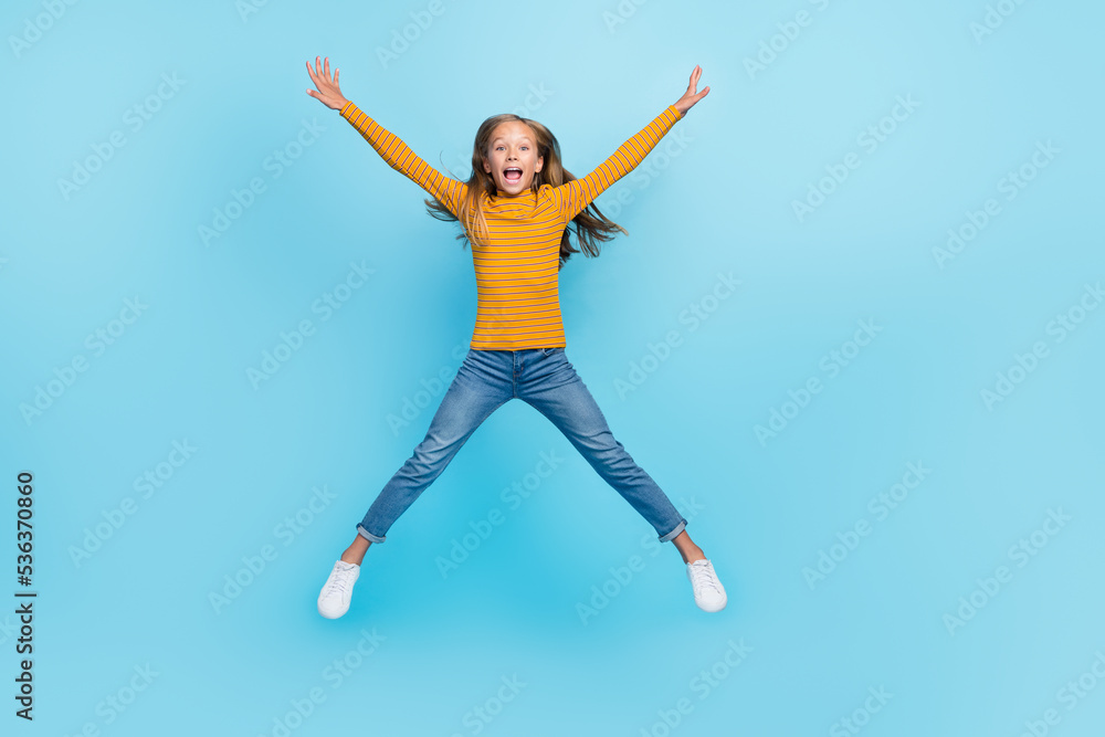 Full size photo of optimistic girl fluttering hairdo dressed yellow pullover denim pants flying jumping isolated on blue color background Full size photo of optimistic girl fluttering hairdo dressed yellow pullover denim pants flying jumping isolated on blue color background