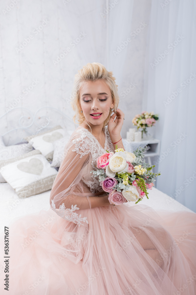 Beauty fashion bride in interior studio with bouquet of flowers in her hands. Beautiful Bride portrait wedding makeup and hairstyle. Fashion bride model in luxury wedding dress.