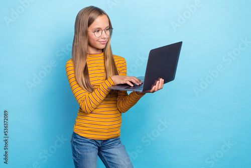 Portrait of clever positive schoolchild hold wireless netbook isolated on blue color background