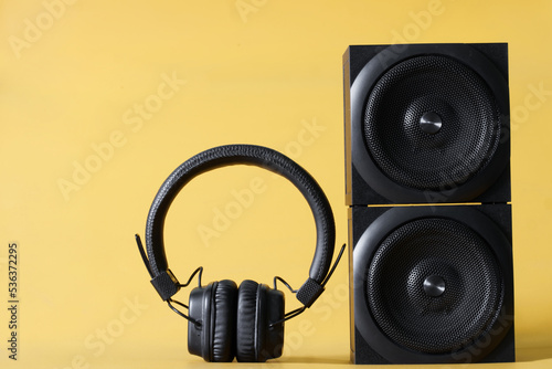 Wireless headphones and two black square audio speakers - an audio system on a yellow background. The concept of listening to music, audio podcasts and internet broadcasts. Copy space. photo