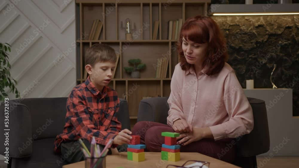 Boy with autism building with wooden blocks doing tasks of autism therapist. School boy with autism studying with teacher. Autism Spectrum Disorder education. Boy with autism building with wooden blocks doing tasks of autism therapist. School boy with autism studying with teacher. Autism Spectrum Disorder education.