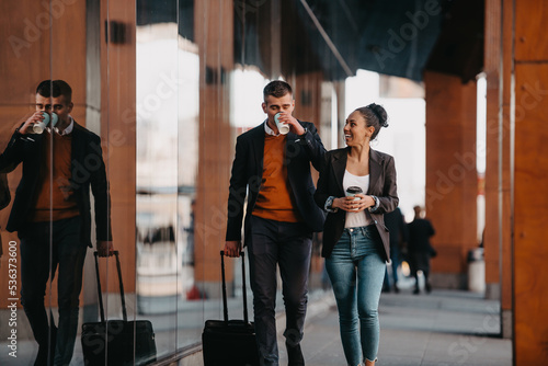 Business man and business woman talking and holding luggage traveling on a business trip, carrying fresh coffee in their hands.Business concept