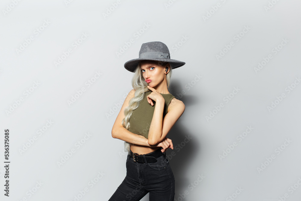Studio portrait of young blonde pretty girl with earbuds in ears, having fun on white background, wearing grey hat. Studio portrait of young blonde pretty girl with earbuds in ears, having fun on white background, wearing grey hat.