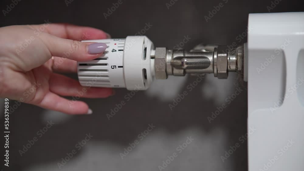 Hand adjusting temperature on heating radiator thermostat, saving energy by adjusting heating thermostat. Hand adjusting temperature on heating radiator thermostat, saving energy by adjusting heating thermostat.