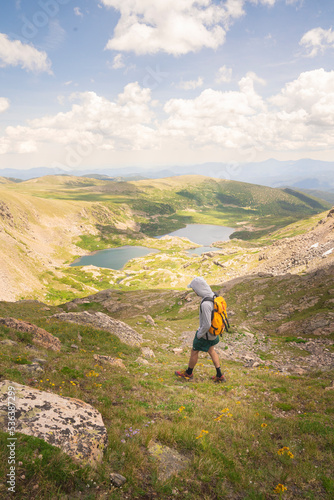 Man with Yellow Backpack Hiking to Alpine Lake with Wildflowers in Colorado Rocky Mountains