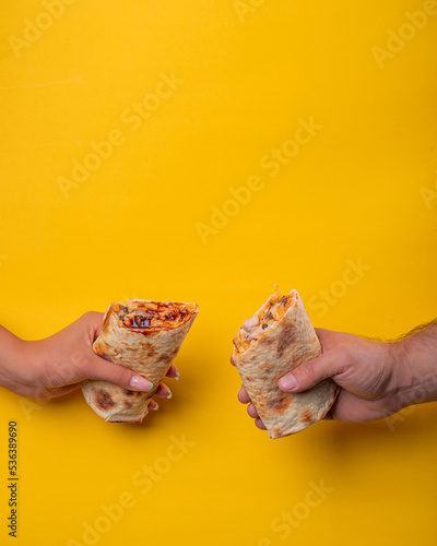 hand holds shawarma. guy with a girl. yellow background