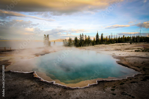Steam coming off of a geyser in Yellowstone National Park - crystal blue water, stunning sky, near sunset.