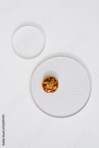 Photo of a delicious modern style handmade mini tart tartlet fulled with differ nuts like pistachio and hazelnut with salted caramel sause on a modern porcelain white flat plate on white background