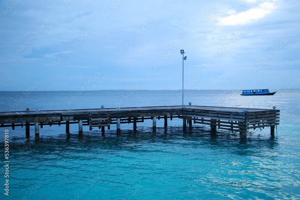 View of the pier and the ocean in the evening on a resort island in the Maldives, the ship is visible on the horizon in the distance