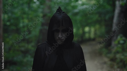 Portrait of a witch in a black cloak with a hood. Woman in the mystical forest. Dark forces photo