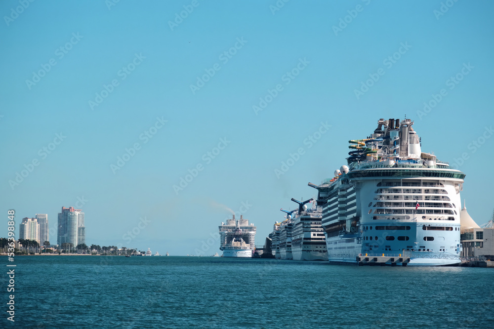 A queue of large cruise ships at the harbor with clear blue sky and a cityscape on the background on Miami Beach, Florida