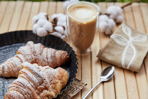 French fresh croissants  cup of latte and cotton at the terrace. Pastel background. Autumn coziness.