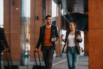 Business man and business woman talking and holding luggage traveling on a business trip, carrying fresh coffee in their hands.Business concept