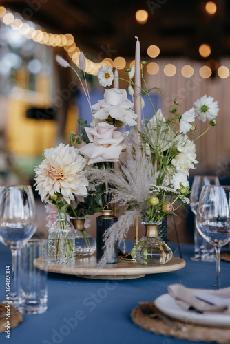 Wedding Decor. Festive table decorated with flowers on the center, candles, silverware and plates with silk napkins on dusty blue tablecloth