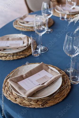 Wedding Decor. Festive table decorated with flowers on the center, candles, silverware and plates with silk napkins on dusty blue tablecloth