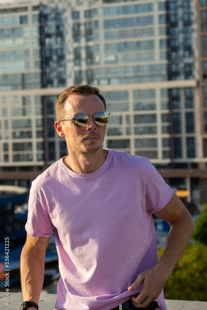 A handsome guy in denim shorts and a pink t-shirt poses beautifully in the city A handsome guy in denim shorts and a pink t-shirt poses beautifully in the city