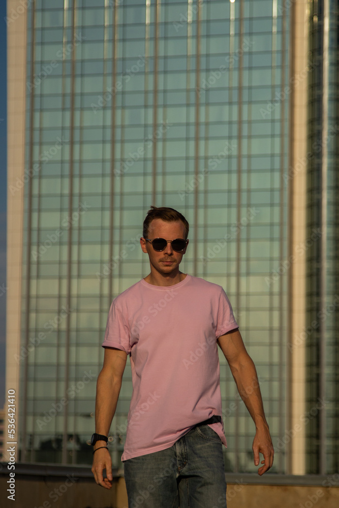 A handsome guy in denim shorts and a pink t-shirt poses beautifully in the city A handsome guy in denim shorts and a pink t-shirt poses beautifully in the city