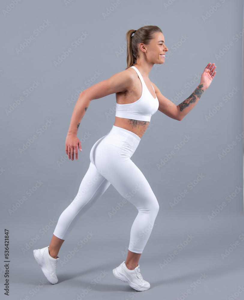 Young fitness woman runner stretching legs before run. Sporty woman runner on gray background. Dynamic movement. Sport and healthy lifestyle. Young fitness woman runner stretching legs before run. Sporty woman runner on gray background. Dynamic movement. Sport and healthy lifestyle.