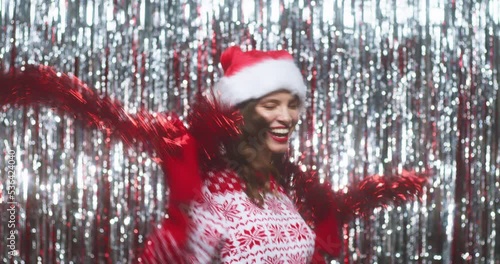 Playful happy young woman in christmas sweater and hat posing and dancing with garland tinsel in hands