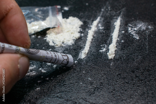 Use from a plastic bag of cocaine through a breathing tube from a hundred dollar bill, on a black background, closeup.