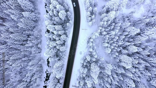 Aerial view on a car driving on winter country road in snowy forest.