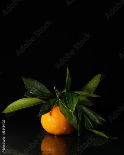 Tangerine with leaves in drops of water on a black background.