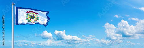 West Virginia - state of USA, flag waving on a blue sky in beautiful clouds - Horizontal banner