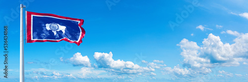 Wyoming - state of USA, flag waving on a blue sky in beautiful clouds - Horizontal banner photo