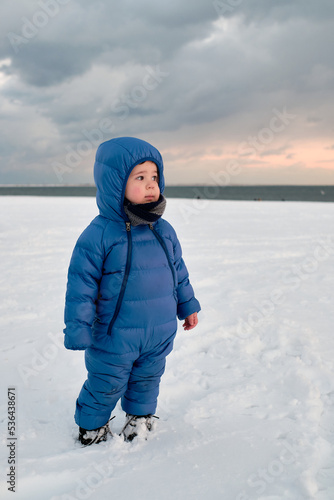 cute baby toddler is playing on a beach covered with snow
