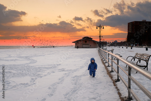 cute baby toddler is running on a beach covered with snow at susnset