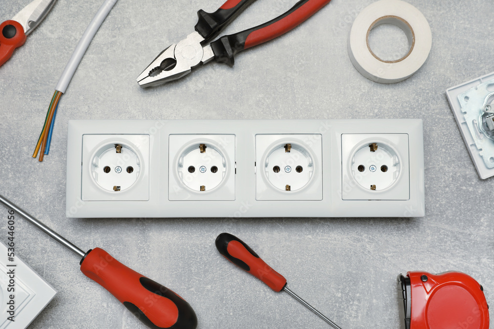 Power socket and set of electrician's tools on grey table, flat lay Power socket and set of electrician's tools on grey table, flat lay