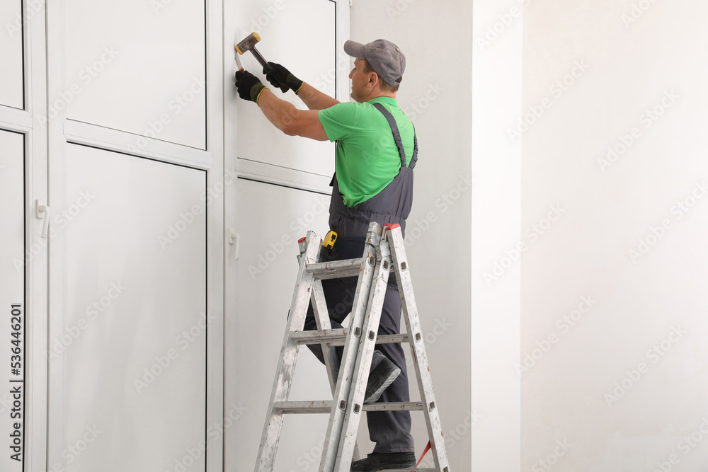 Worker on folding ladder installing window indoors