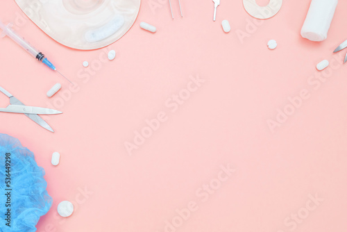 A colostomy bag, pills, medical instruments, a bandage and a medical cap on a pink background. photo