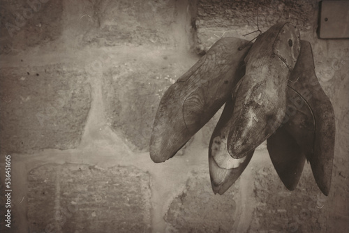 Antique wooden cobbler shoe molds needed to make shoes hang on an old stone wall. Shoe Making Repairing