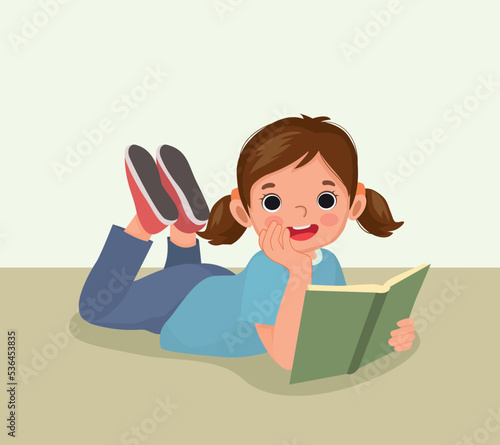 Cute little girl reading book lying on floor