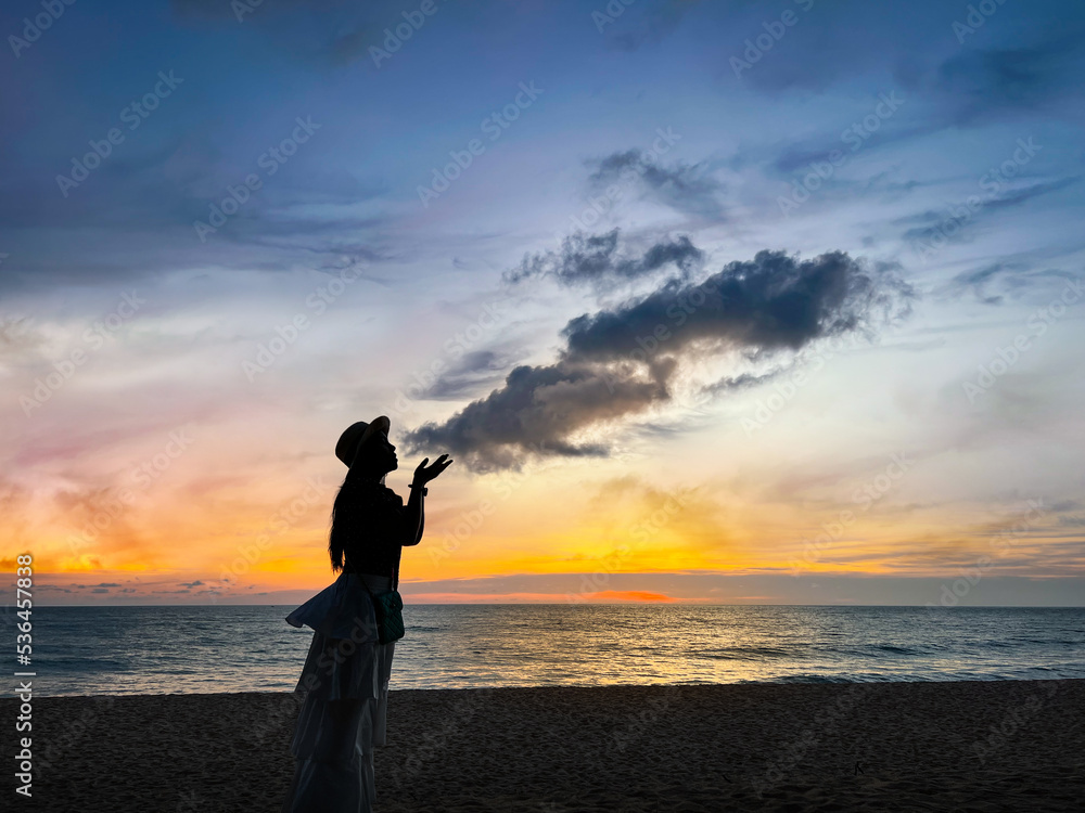 Abstract, Scene of the sunset silhouette, Alone woman on the beach at twilight come to travel to relax at sea on summer vacation, she blowing clouds in the sky. Khao Lak Beach, Phang Nga, Thailand.