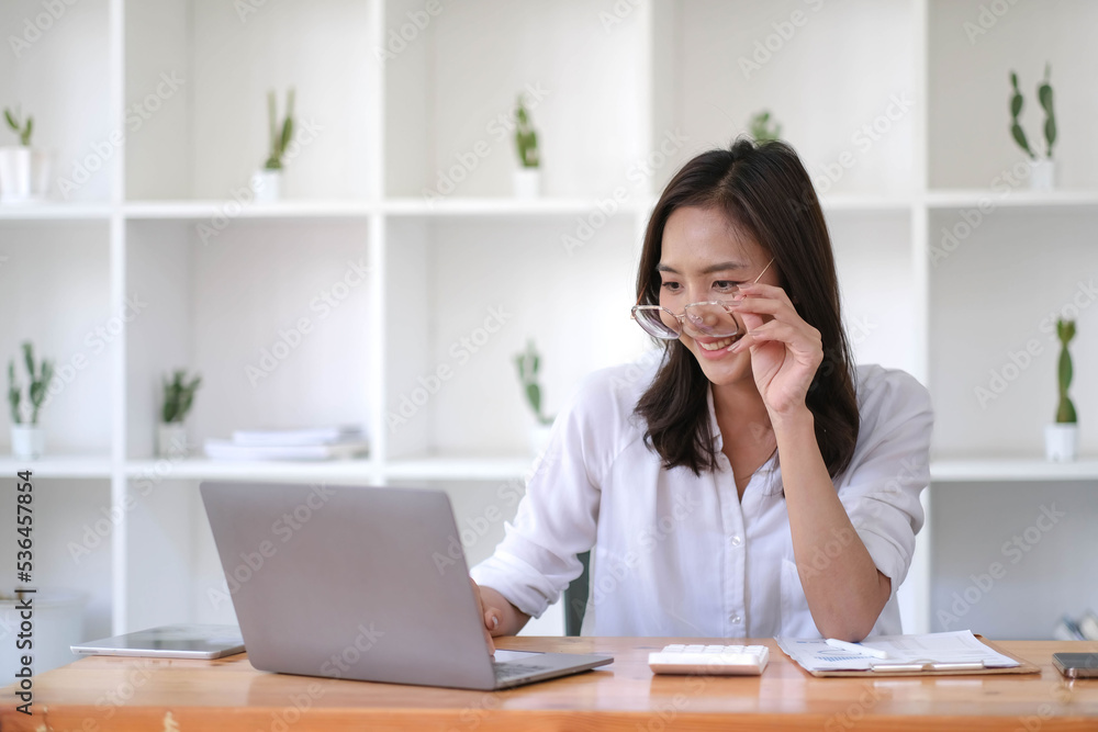 Beautiful smiling Asian businesswoman wearing glasses hand holding pen working using laptop at office. Beautiful smiling Asian businesswoman wearing glasses hand holding pen working using laptop at office.