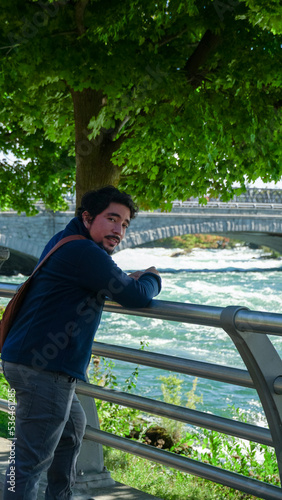 Joven adulto hispano posando cerca de un rio en un dia soleado. Parque natural de Niagara Falls 