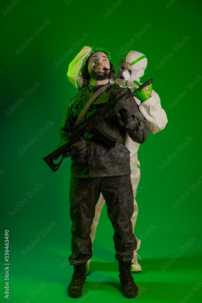 a soldier in a studio on a green background with a medic or scientist in a white protective suit. a man in military uniform rifle or machine gun carries a person in chemical protection on his shoulder a soldier in a studio on a green background with a medic or scientist in a white protective suit. a man in military uniform rifle or machine gun carries a person in chemical protection on his shoulder